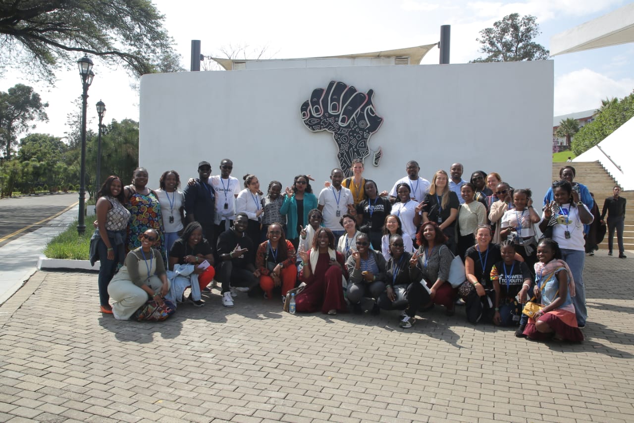 Power to You(th) colleagues posing for a picture below a black and white mural doodling of the African map.